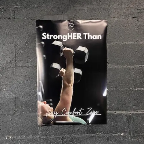 A sign showing a woman lifting dumbells with the text "StrongHER Than My Comfort Zone" 